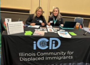 Rosa and Evelyn at the ICDI Table with our logo on the front and materials arranged.